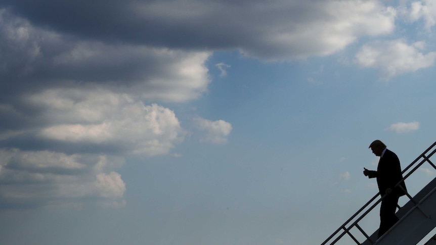 US President Donald Trump walks down stairs off an airplane with storm clouds in the distance