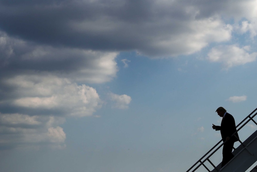 US President Donald Trump walks down stairs off an airplane with storm clouds in the distance