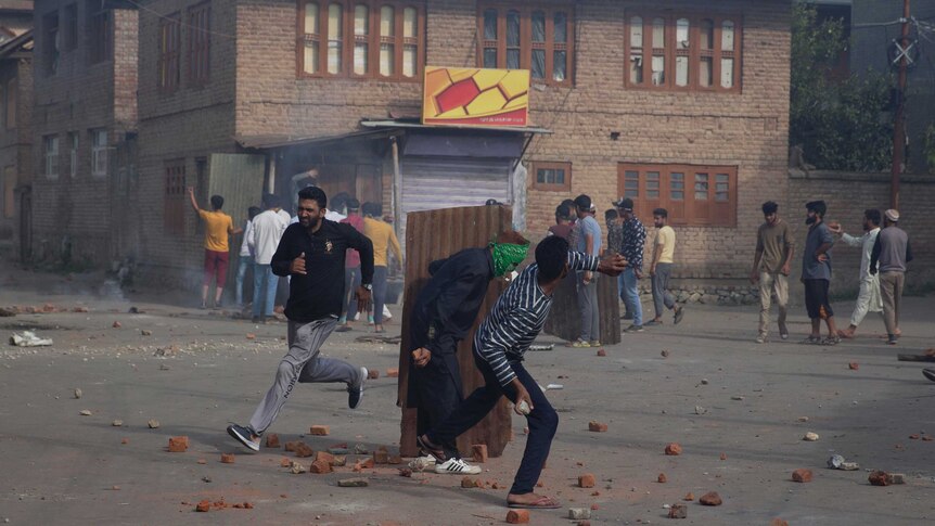 Men crouch behind metal barrier while throwing rocks