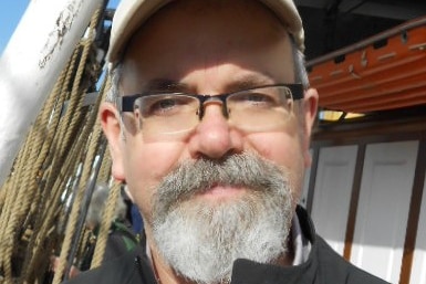 A man wearing glasses and a cap, with a grey beard.