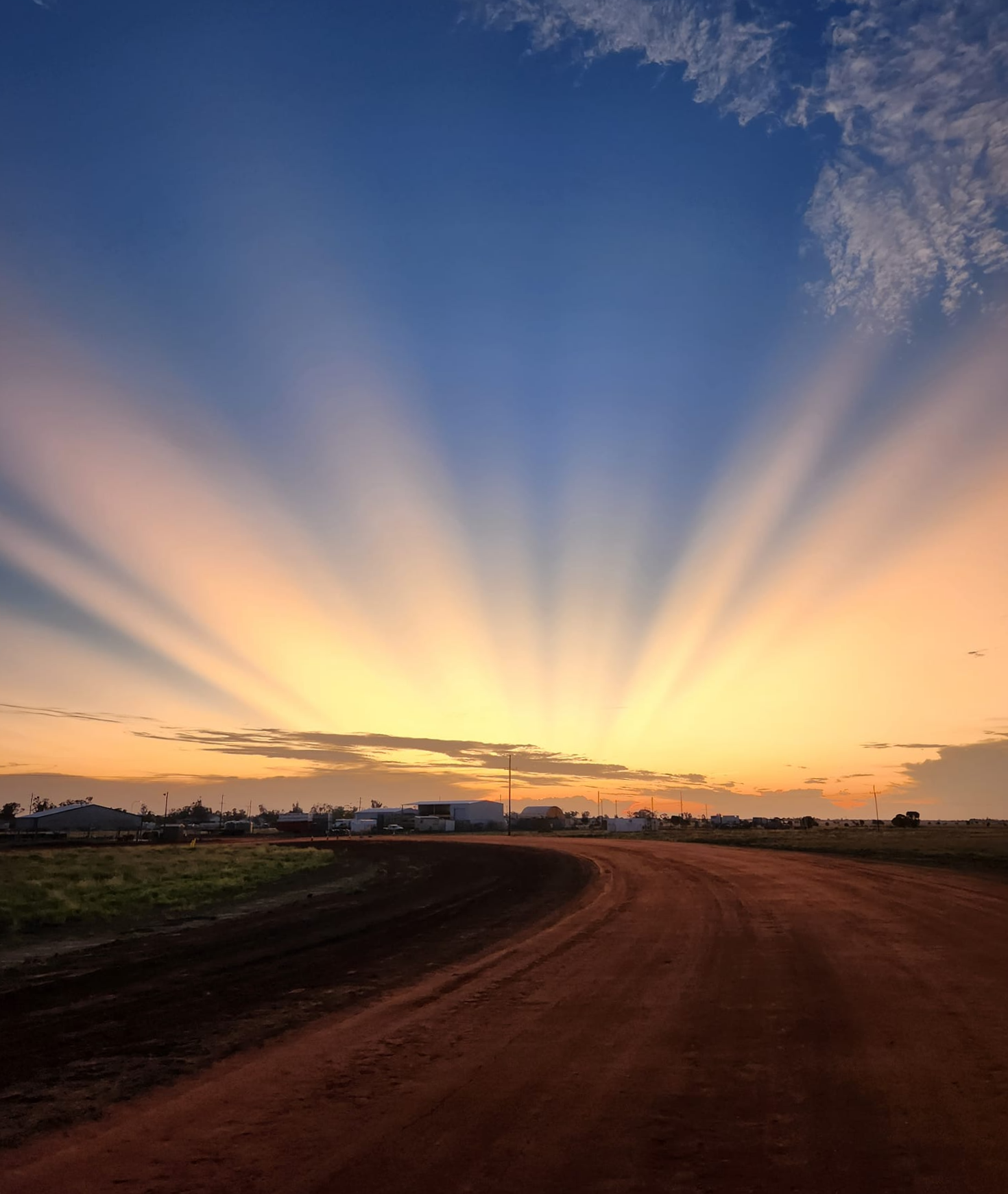 Rays of sunlight over a dirt road leading into a country town. 
