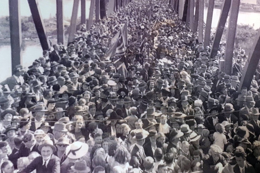 A black-and-white photo shows a large group of people huddled on a bridge.
