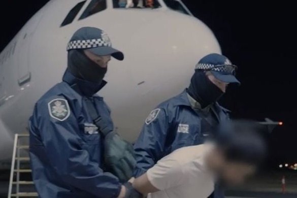 Two AFP officers with their faces covered escort a man across the tarmac of an airport at night.