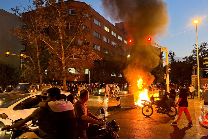 A motorcycle burns as protesters and people in cars and motorcycles pass by