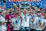 Sydney Fc players celebrate with the A-League trophy as confetti flies around in the air.