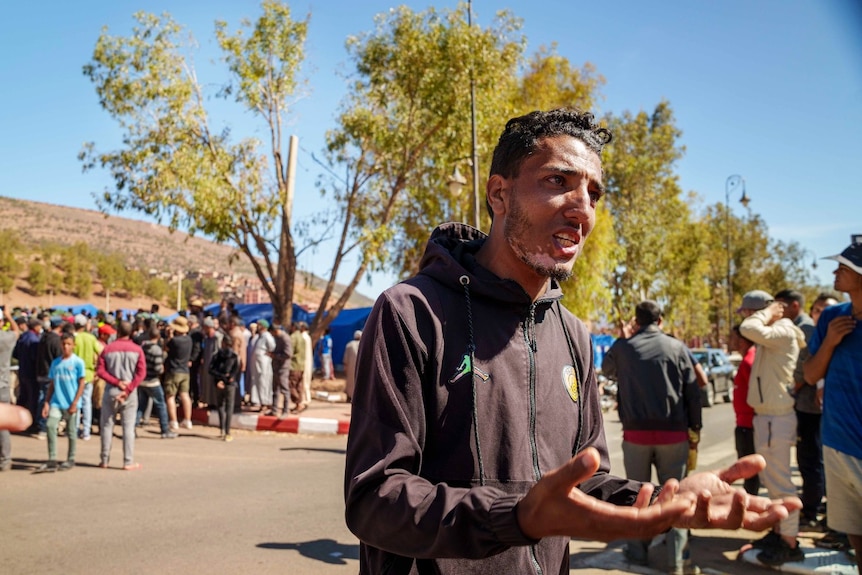 A man gestures with his arms out as a large crowd stands behind him