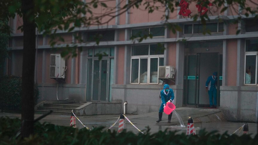 Hospital staff wash Wuhan hospital entrance, using a bucket and wearing protective clothing.
