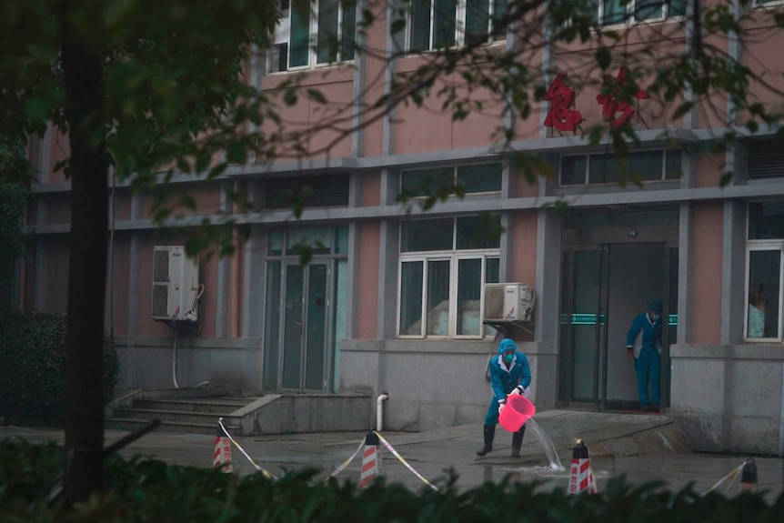 Hospital staff wash Wuhan hospital entrance, using a bucket and wearing protective clothing.