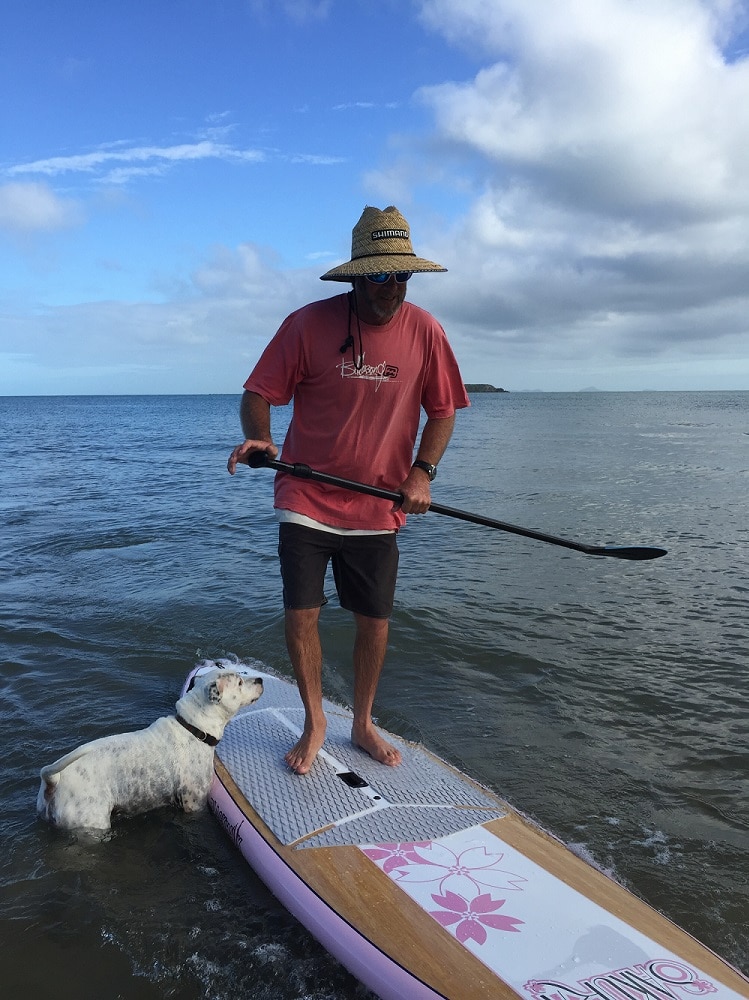 A dog stands next to a man who is paddleboarding