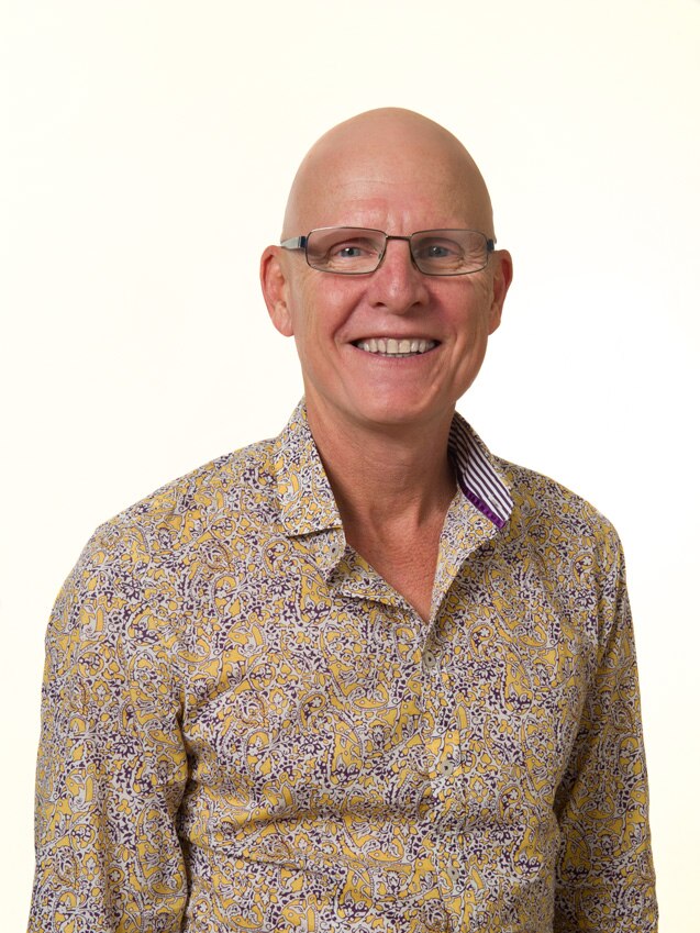 A bald man wearing glasses and a colourful shirt.