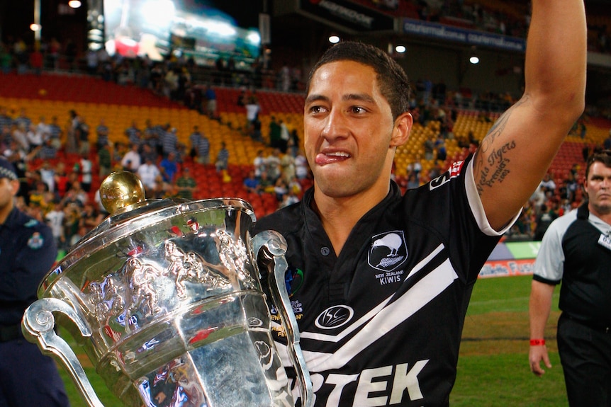 Benji Marshall holds a silver trophy under his right arm and raises his left arm above his head