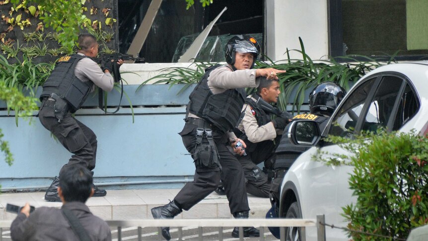 Police aim and take their positions as their pursue suspects outside Starbucks after a series of blasts in Jakarta, Indonesia