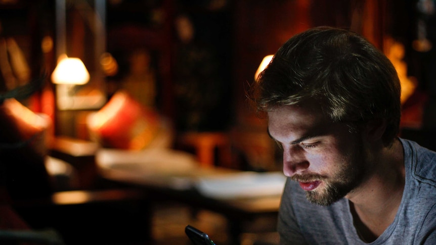 Man looking at phone in dark room for a story on making Instagram more positive