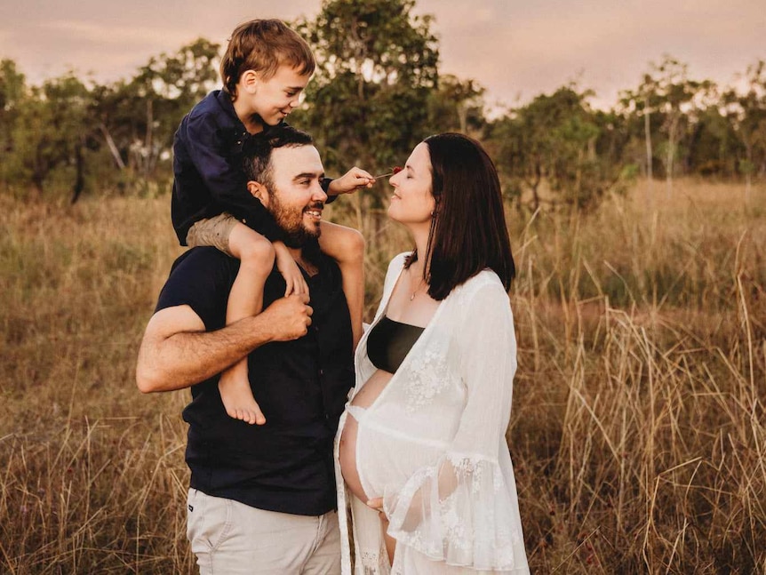 Pregnant woman stands in field with man and child