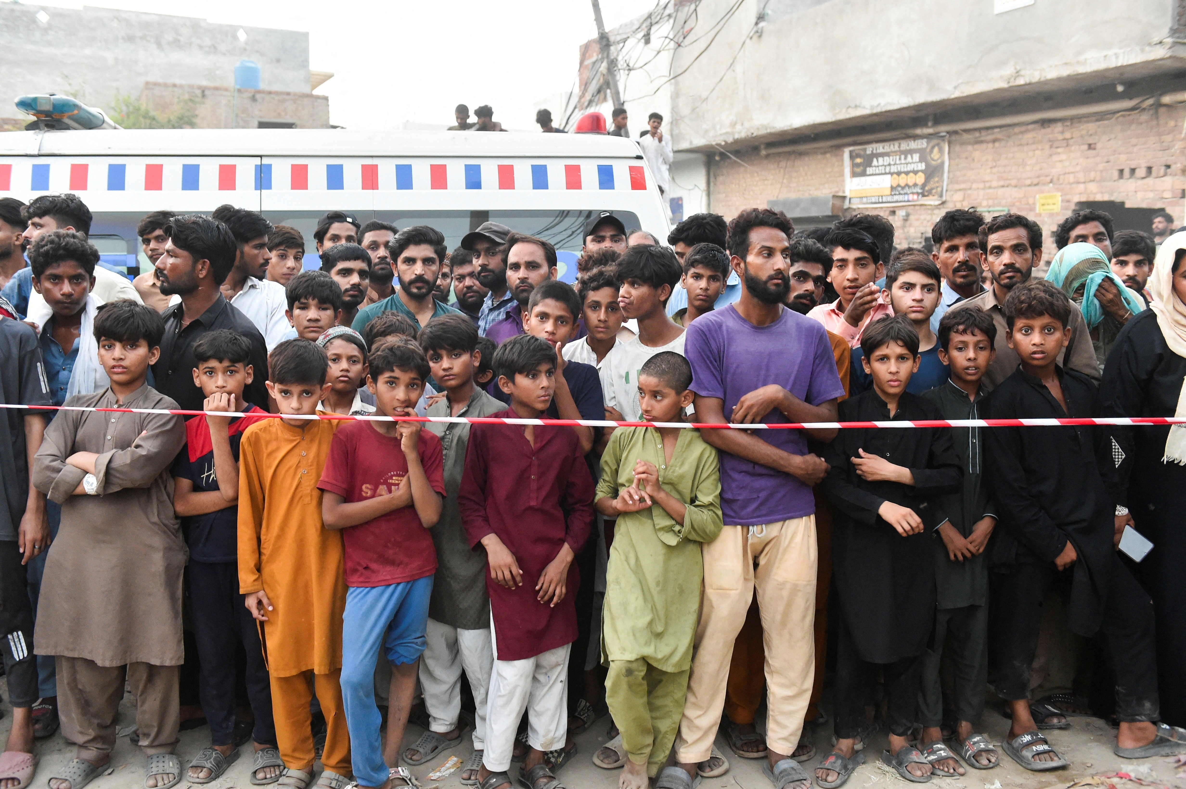 young children stand beside red and white tape cordoning off an area.
