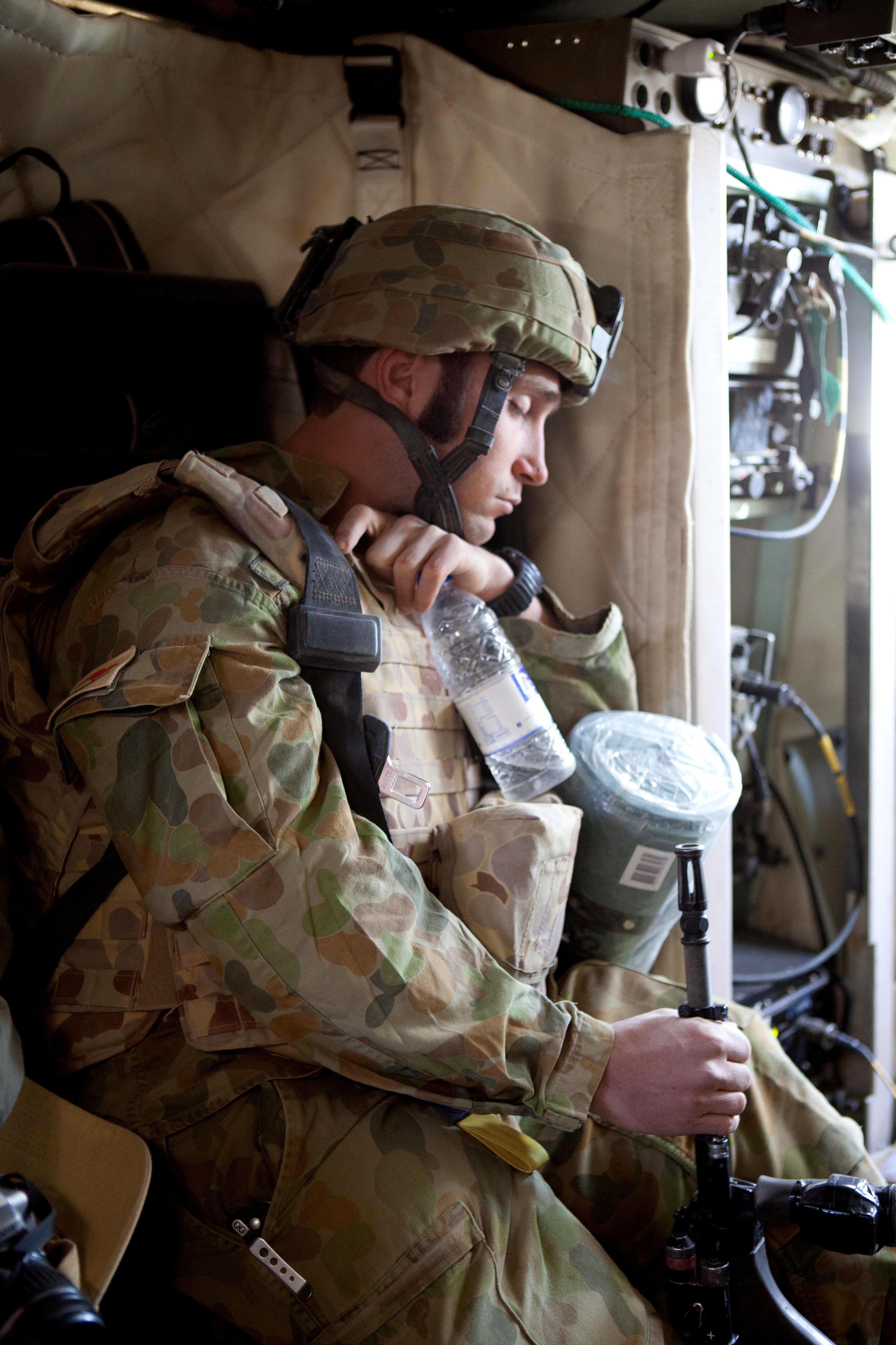 A photograph of an Australian soldier wearing army greens and a helmet while sleeping.