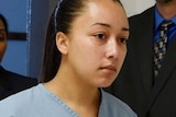 Cyntoia Brown wears blue prison-issued shirt and jeans as she walks through hall with hands cuffed, accompanied by two people.