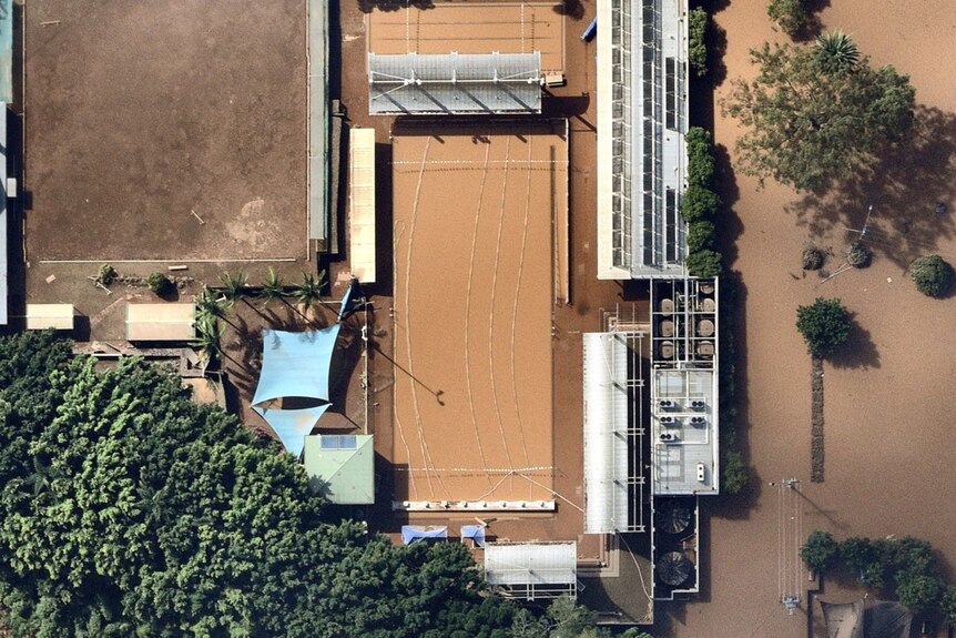 An aerial view of a public swimming pool that is now brown with floodwater.