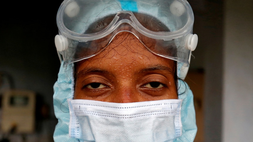 A woman in goggles and a white face mask with beads of sweat on her forehead