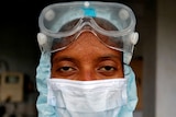 A woman in goggles and a white face mask with beads of sweat on her forehead