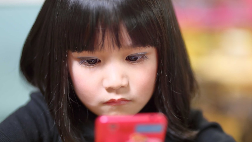 A young girl looks at a smartphone.