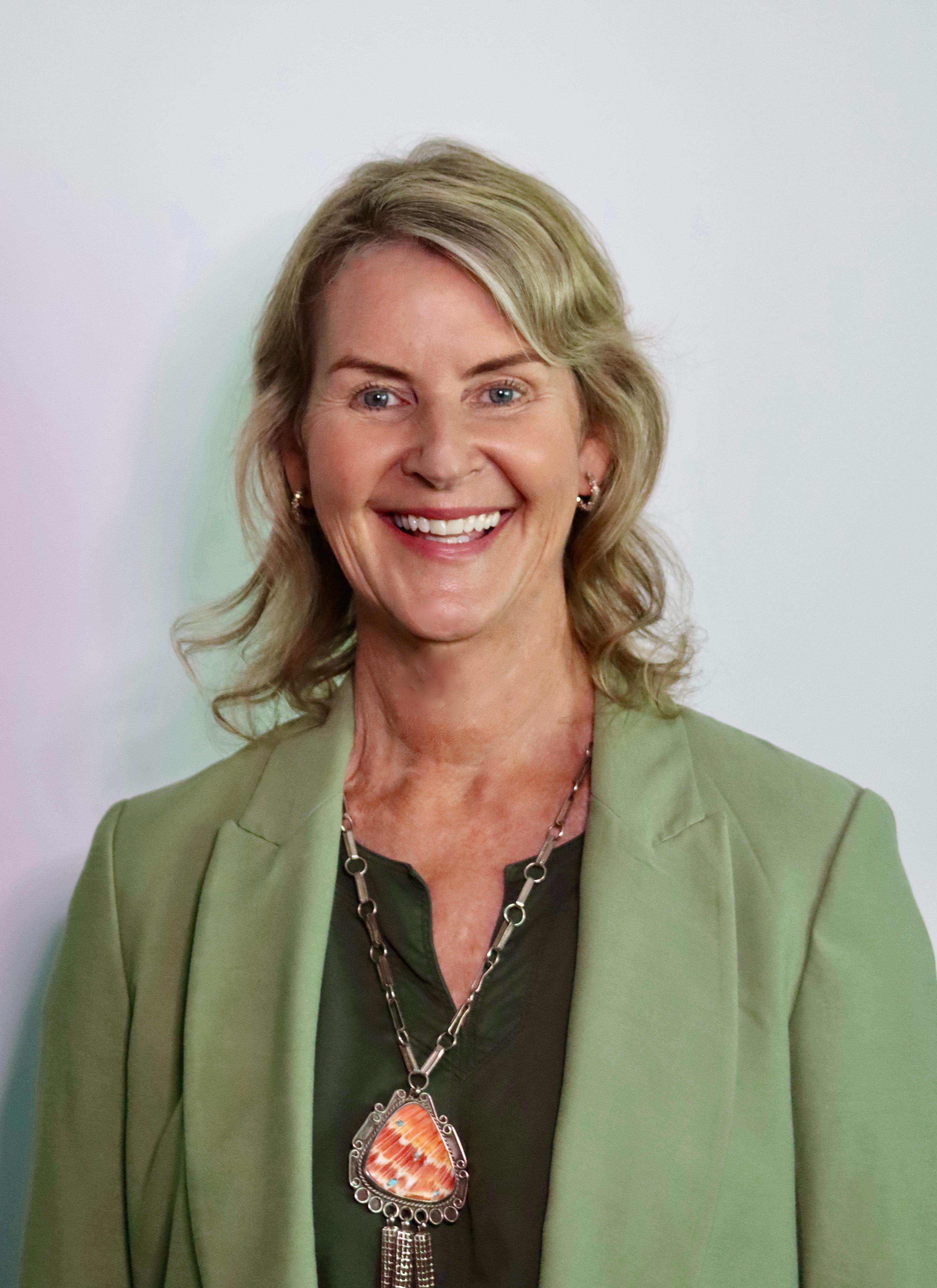 Waring a green jacket and large necklace, Melanie smiles at the camera