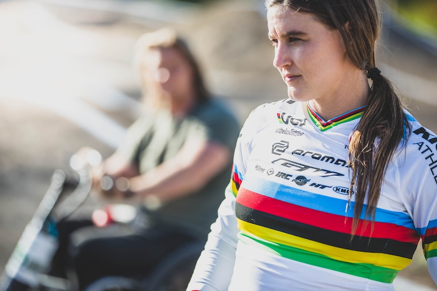 Alise wears a rainbow jersey in the foreground with Sam in wheelchair in background