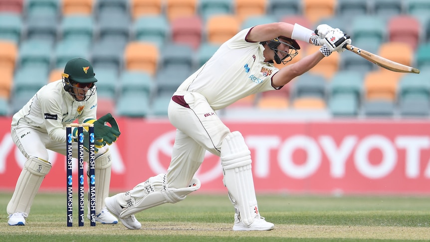 Batsman taking a swing at the ball with the wicket-keeper crouched behind him