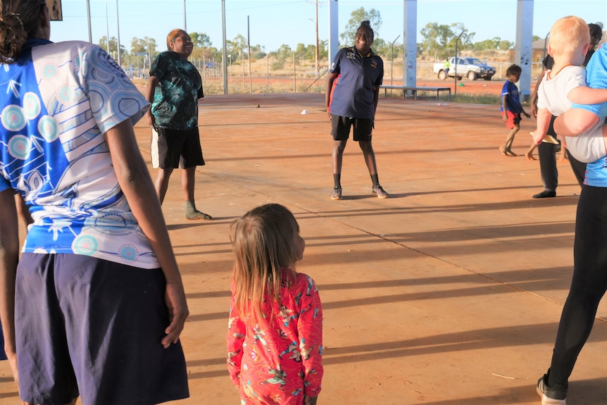 A group of women and kids are training on a basketball court.