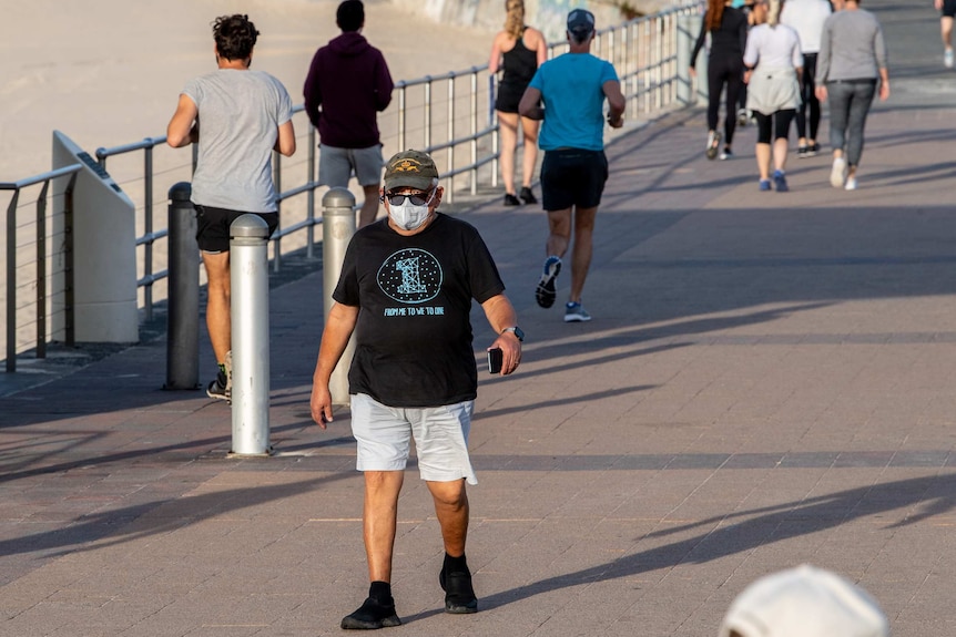 A man walking along Bondi promenade wearing a protective mask.