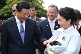 Xi Jinping and pats a Tasmanian devil behind held by his wife. Behind is an entourage including interpreter Charles Qin