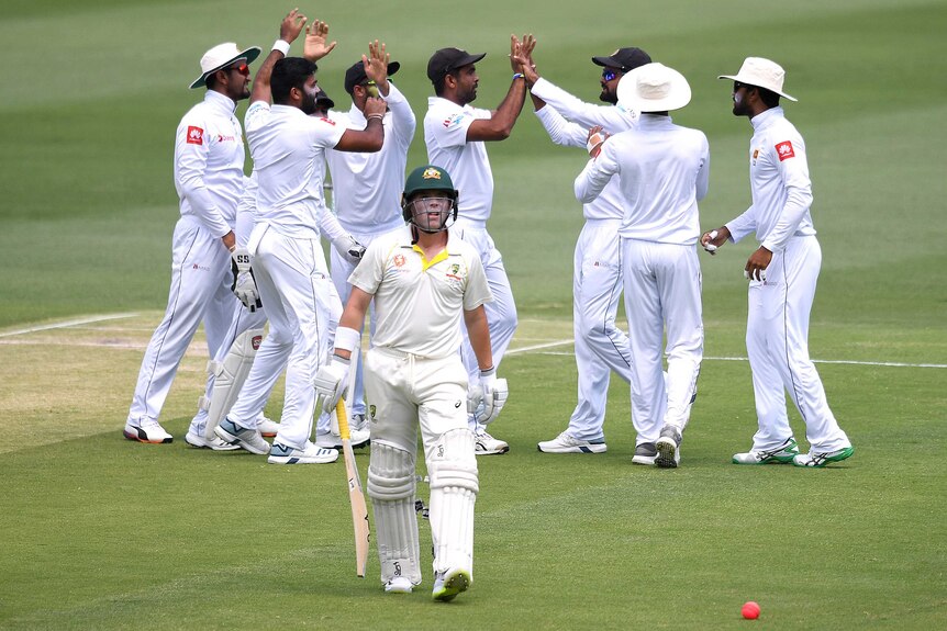Marcus Harris walks off bat in hand and helmet on as Sri Lankan players celebrate behind him.