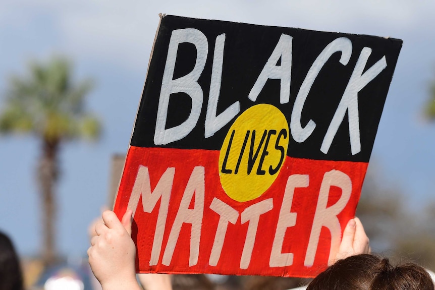 A close up image of a sign saying Black Lives Matter using the design of the Aboriginal flag.