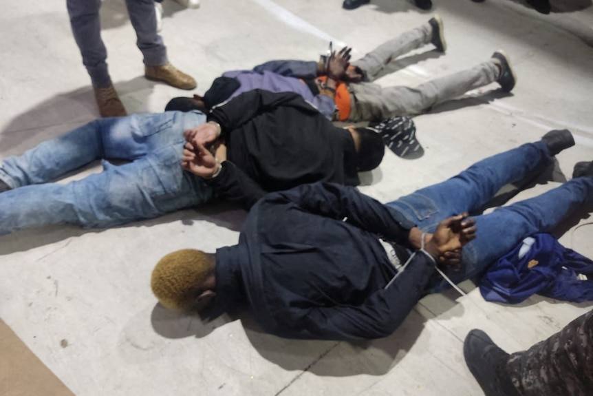 Photo of men ziptipped and lying on the ground. 