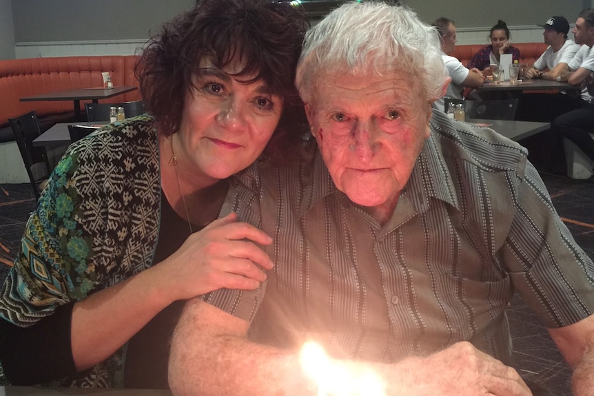 Woman poses for a photo with her elderly father with his birthday cake 