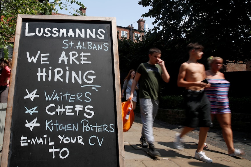 People walk past a sign that reads 'we are hiring waiters, chefs, kitchen porters'