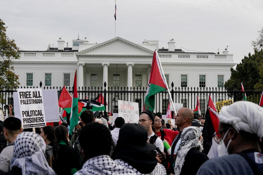 Palestinian flags and signs are held up by a large crowd in front of the White House.