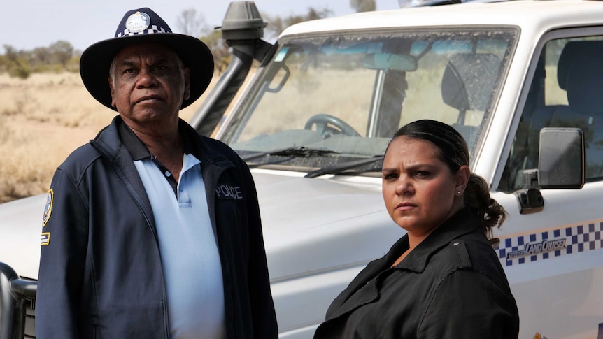 actors warren Hi Williams in police uniform and Rarriwuy hick in front of a police wagon