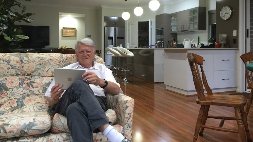 A man in his eighties sits on a couch in his living room