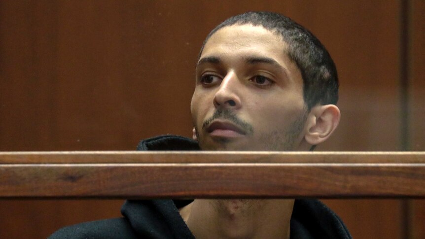 Tyler Barriss peers over a bar while sitting in the Los Angeles Superior Court, wearing a hoodie.