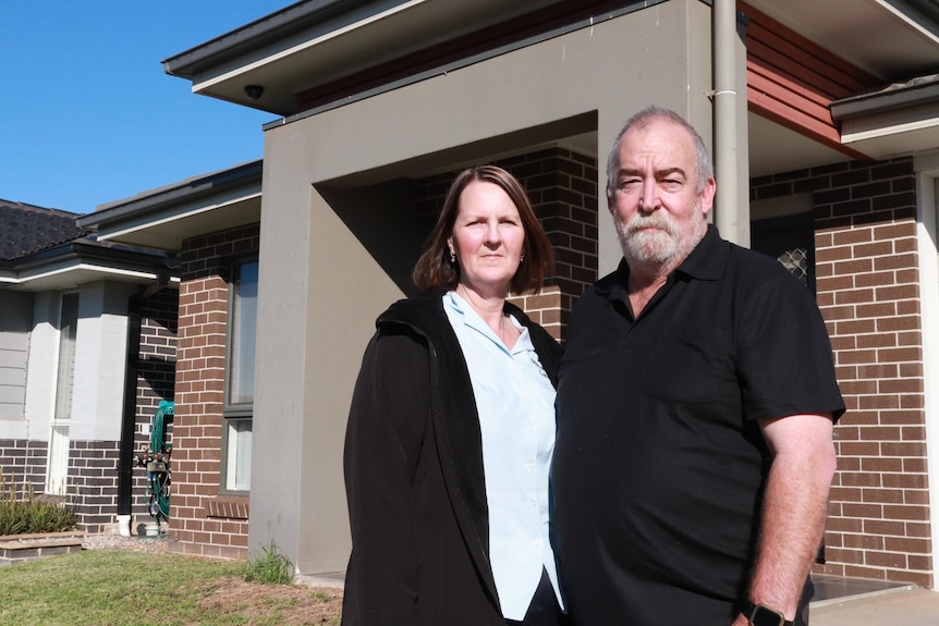 A concerned couple stands outside their house