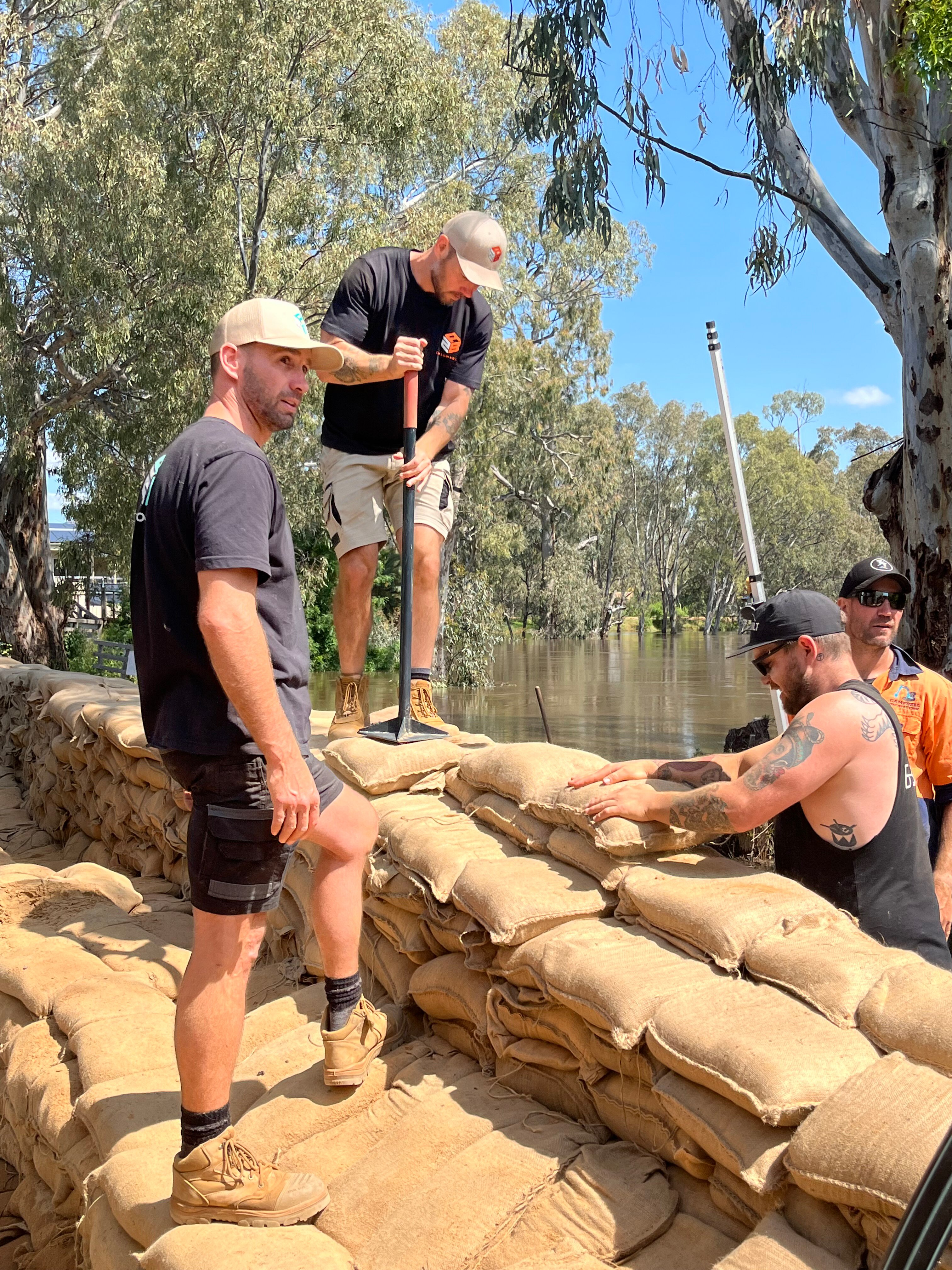 Four men building a sandbag wall near a river.