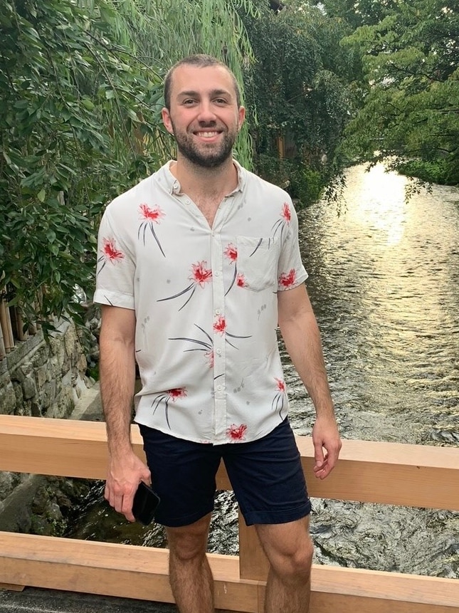 Jake Wheeler posed for a photo on a bridge overlooking a river.