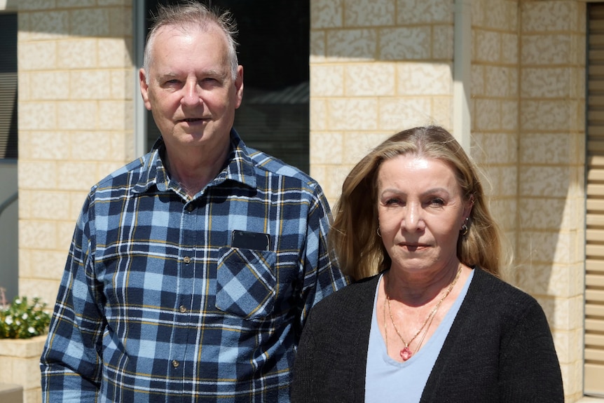 A man and woman stand outside a house.