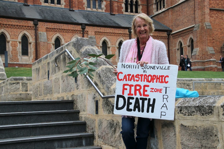A woman standing outside St George's Cathedral holds a sign in protest against the Stoneville development.