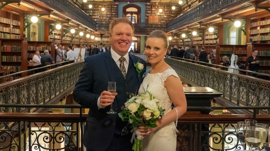 Richard Boyle wears a navy suit and Louise Beaston wears a white wedding dress.