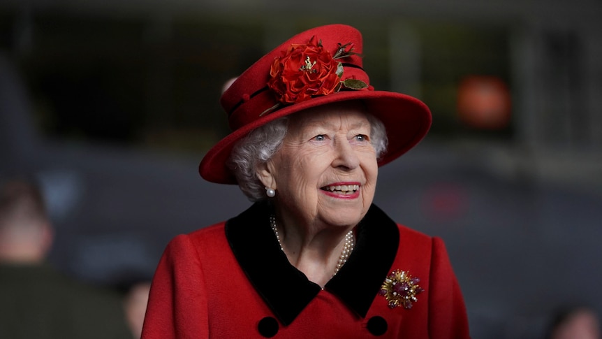 The Queen smiles while wearing a bright red hat and coat.