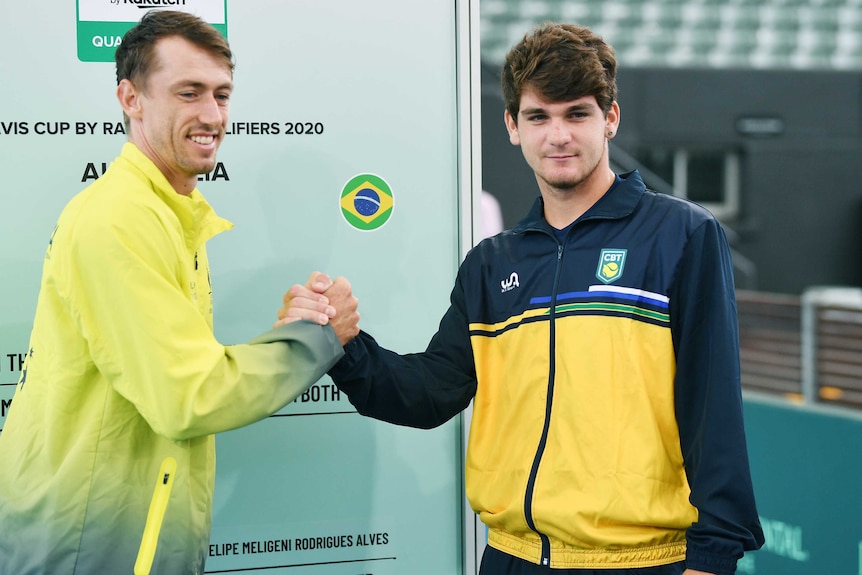 Australian and Brazilian tennis players shake hands in front of board showing a Davis Cup tie draw.
