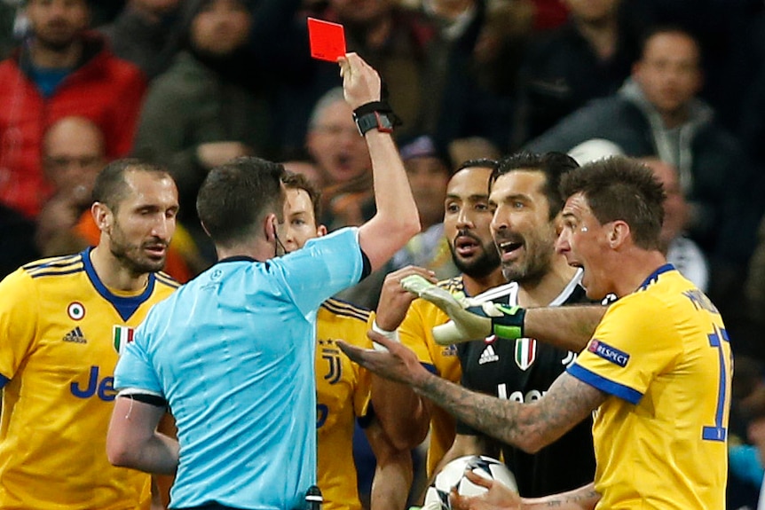 A referee shows a red card to goalkeeper Gianluigi Buffon while surrounded by Juventus players