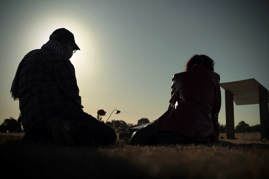 Janna and Hazim Al-Umari backlit by the sun as they sit by their son's grave